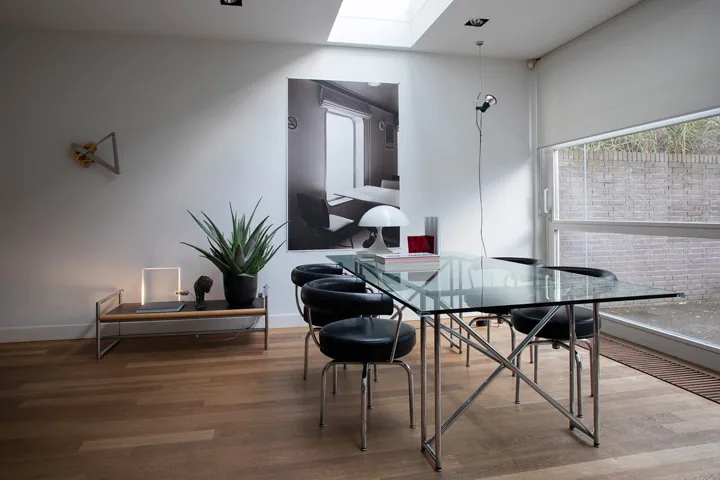 Eethoek met glazen tafel en zwartleren designstoelen bij een raam met tuinzicht