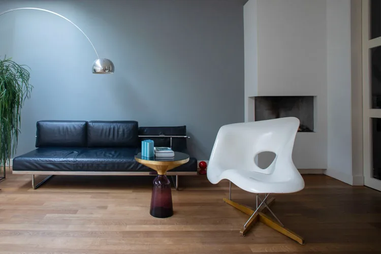 Woonhoek met zwartleren daybed, witte loungestoel en booglamp bij een open haard