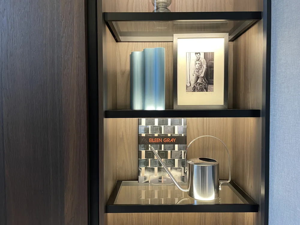 Gestileerde wandkast met metalen vaas, fotolijst en designboek op houten planken